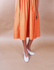 Woman wearing a orange pleated Anissa Mpungwe dress against a beige background