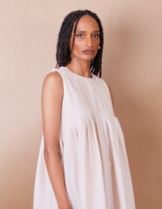 Woman wearing a white pleated Anissa Mpungwe dress against a beige background