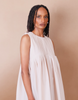 Woman wearing a white pleated Anissa Mpungwe dress against a beige background