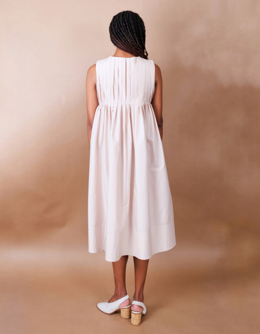 Woman wearing a white pleated Anissa Mpungwe dress against a beige background