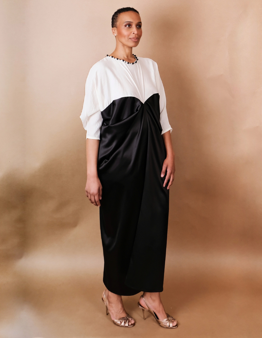 Woman wearing a two-tone dress with a white top and black skirt against a beige background